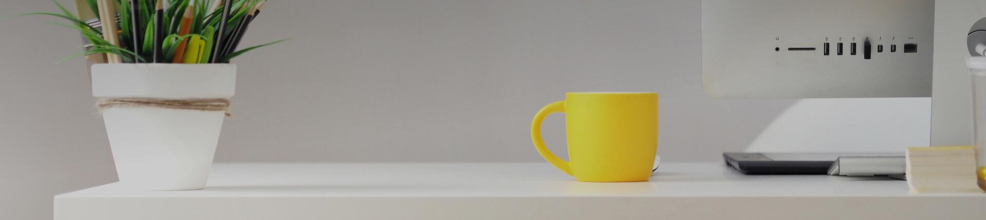 Pflanze, Tasse und Mac auf Schreibtisch